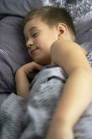 une mignonne caucasien garçon de 5 ans vieux est en train de dormir dans lit photo