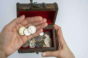 une petit vieux en bois poitrine et femelle mains compte pièces de monnaie sur une blanc Contexte photo