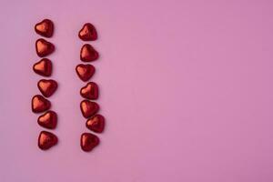 deux ruisseaux de cœurs sur brillant de fête rose Contexte avec brillant des sucreries dans le forme de cœurs enveloppé dans déjouer photo