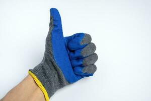 une homme main dans bleu caoutchouté travail gants spectacles une les pouces en haut sur une bleu Contexte photo