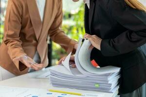 femme d'affaires mains travail sur piles de papier les documents à chercher et la revue les documents empilé sur table avant Envoi en cours leur à planche de réalisateurs à utilisation correct les documents dans réunion avec homme d'affaire photo