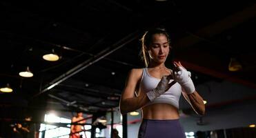 portrait de femme apprentissage muay thaïlandais à construire en haut le force de le corps et utilisation il pour auto défense. sont en utilisant main enveloppements avant en mettant sur boxe gants pour boxe photo