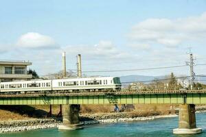 fermer blanc train est traversée une rivière par le pont en dessous de brillant bleu ciel avec coton nuage. photo