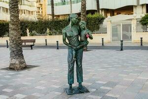 bmétal statue de une femme avec une fille en portant une réel fleur par le plage dans Alicante, Espagne photo