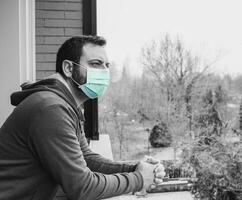 Jeune caucasien homme avec masque à la recherche en dehors sur Accueil terrasse pendant quarantaine dû à coronavirus covid19 pandémie. photo