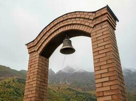 Stock photo de ancien cuivre ou bronze cloche pendaison sur une pierre Cadre à chapelle dans honneur de le mort sur brumeux Montagne Contexte. image capturé à irafski district, Stur-digora village. Russie.