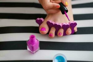 le enfant des peintures le sien les ongles avec brillant violet vernis. peu fille Est-ce que une pédicure. beauté salon jeu. enfants divertissement. photo