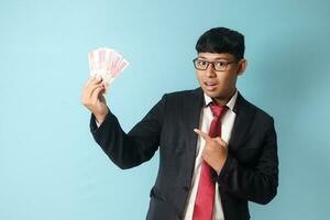 portrait de Jeune asiatique affaires homme dans décontractée costume avec surpris expression montrant mille roupies.isolé image sur bleu Contexte photo