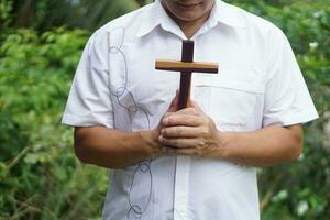 fermer asiatique homme Christian détient en bois traverser et prie Extérieur dans le soir. concept , Christian culte. foi, pardon, croyance, l'amour et espoir. religieux symbole de christianisme. photo