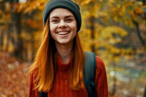 portrait de une magnifique femme dans une chapeau chandail avec une sac à dos sur sa retour dans le l'automne forêt dans la nature photo