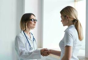 une femme médecin dans une médical robe écoute à le problèmes de une patient dans une blanc T-shirt photo