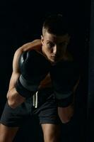 boxeur dans noir gants courbé vers le bas sur une foncé Contexte bodybuilder aptitude faire des exercices photo