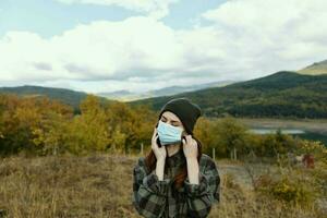 femme dans une médical masque et dans une chaud chapeau l'automne feuilles des arbres montagnes photo