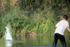 asiatique garçon dans blanc T-shirt est dépenses le sien temps libre par plongée, natation, lancement rochers et contagieux poisson dans le rivière Heureusement, loisir et bonheur de les enfants concept, dans mouvement. photo