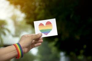 cœur arc en ciel couleurs carte en portant dans main lequel a arc en ciel bracelet autour il, concept pour donnant l'amour et attrayant tout gens à célébrer lgbt événements dans fierté mois. photo