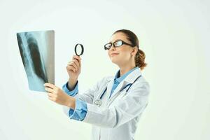 une infirmière dans une blanc manteau regards à un radiographie par une grossissant verre photo