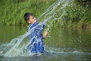 asiatique garçon dans bleu T-shirt est dépenses le sien temps libre par plongée, natation, lancement rochers et contagieux poisson dans le rivière Heureusement, loisir et bonheur de les enfants concept, dans mouvement. photo