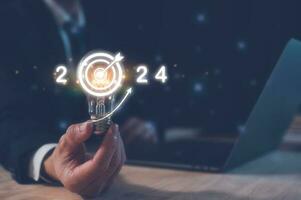 2024 affaires Planification et stratégie concept, homme d'affaire en portant lumière ampoule avec le année 2024 cible fléchettes, commercialisation financier et recherche analyse, investissement les tendances suivant Nouveau année photo