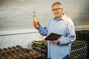 portrait de Sénior homme qui possède vignoble. il est examiner qualité dans le sien du vin cave. industrie du vin fabrication concept. photo