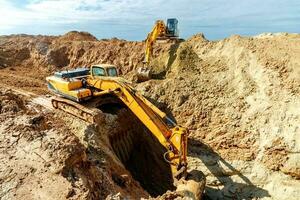 deux excavatrice sont creusement sol dans le construction site sur ciel arrière-plan, avec blanc duveteux nuage photo