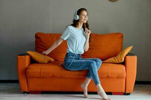 magnifique femme écoute à la musique avec écouteurs sur le Orange canapé inchangé photo