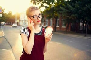 femme avec court cheveux sur le rue parlant sur le téléphone une tasse de boisson photo