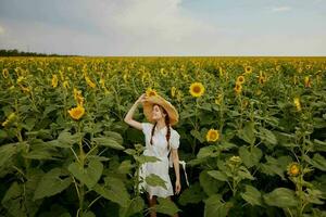 femme avec deux nattes dans une blanc robe en marchant sur une champ de tournesols été temps photo