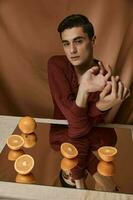 une Beau homme dans une rouge chemise est assis à une table dans de face de une miroir avec des oranges photo