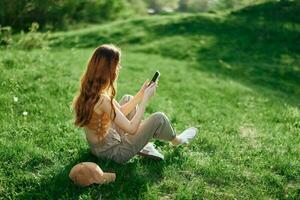 free-lance étudiant travail sur le téléphone séance en plein air dans le été sur vert herbe, mobile et l'Internet en dehors de ville photo