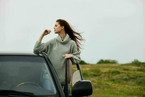 jolie femme avec rouge cheveux dans une chandail près le voiture la nature inchangé photo