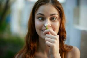 marrant femme à la recherche à une petit fleur dans sa main avec sa yeux plissé. photo