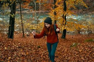 femme dans une chandail avec une sac à dos repos dans une parc près le rivière dans la nature dans l'automne photo