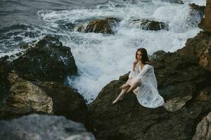 pieds nus femme dans blanc robe est assis sur une pierre avec humide cheveux inchangé photo