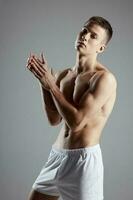 homme bodybuilder dans blanc short faire des gestes avec mains sur gris Contexte sport aptitude photo