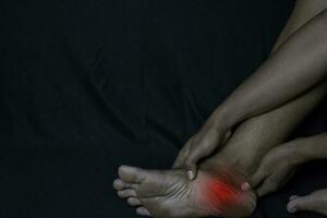 asiatique homme en portant le sien pied. il se sent douleur pied talon avec noir Contexte. plantaire fascilite. médical ou soins de santé concept photo