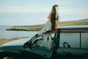 femme avec rouge cheveux dans une chandail près le voiture la nature femelle relaxant photo