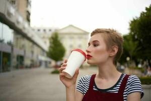 femme avec court cheveux sur le rue portant des lunettes verre avec boisson marcher photo