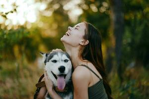 une femme avec une rauque race chien sourit et affectueusement coups sa bien-aimée chien tandis que en marchant dans la nature dans le parc dans l'automne contre le toile de fond de le coucher du soleil photo