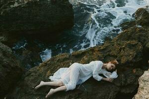 magnifique la mariée dans longue blanc robe humide cheveux mensonge sur une rocheux falaise inchangé photo