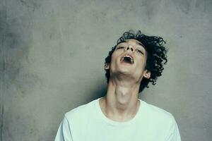 de bonne humeur gars avec frisé cheveux s'incline le sien tête à le côté sur une gris Contexte studio de photographie modèle photo