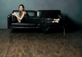 un élégant Dame dans une noir robe mensonges sur une cuir canapé à l'intérieur dans plein croissance photo