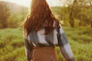 une femme court à travers une champ avec sa retour à le caméra sur une été journée avec sa cheveux longue et en volant dans le le coucher du soleil. le concept de liberté et harmonie avec la nature photo
