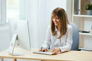 de bonne humeur content adorable blond femme d'affaires ouvrier pigiste Regardez à écran travail sur bureau ordinateur en ligne dans lumière moderne bureau. content employé écrit trimestriel rapport. copie espace, éloigné emploi photo