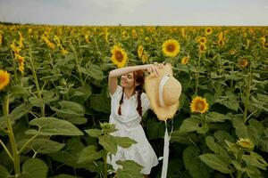 magnifique sucré fille dans une paille chapeau dans une blanc robe une champ de tournesols agriculture paysage photo