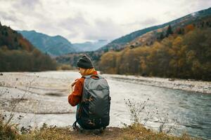 femme avec une sac à dos et dans une veste avec une chapeau sur le rivière banque dans le montagnes dans la nature photo