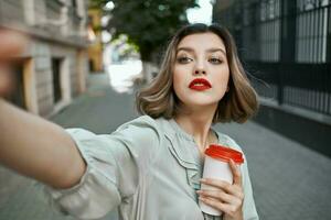 de bonne humeur femme prise une selfie sur le rue avec une tasse de café photo