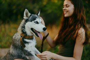 une femme avec une rauque race chien sourit et affectueusement coups sa bien-aimée chien tandis que en marchant dans la nature dans le parc dans l'automne contre le toile de fond de le coucher du soleil photo