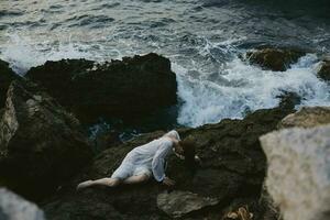 magnifique Jeune femme dans une isolé place sur une sauvage rocheux côte dans une blanc robe été vacances concept photo