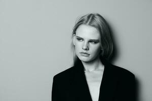 fermer portrait de pensif sérieux blond modèle dans noir veste posant penché sur le studio mur. élégant minimaliste tirer photo