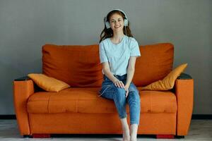 femme sur le Orange canapé écoute à la musique avec écouteurs les technologies photo